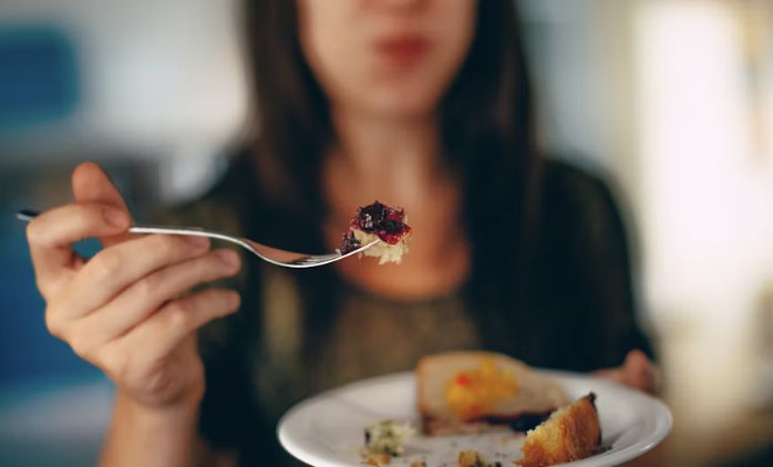 Mulher a segurar um garfo com comida, em primeiro plano